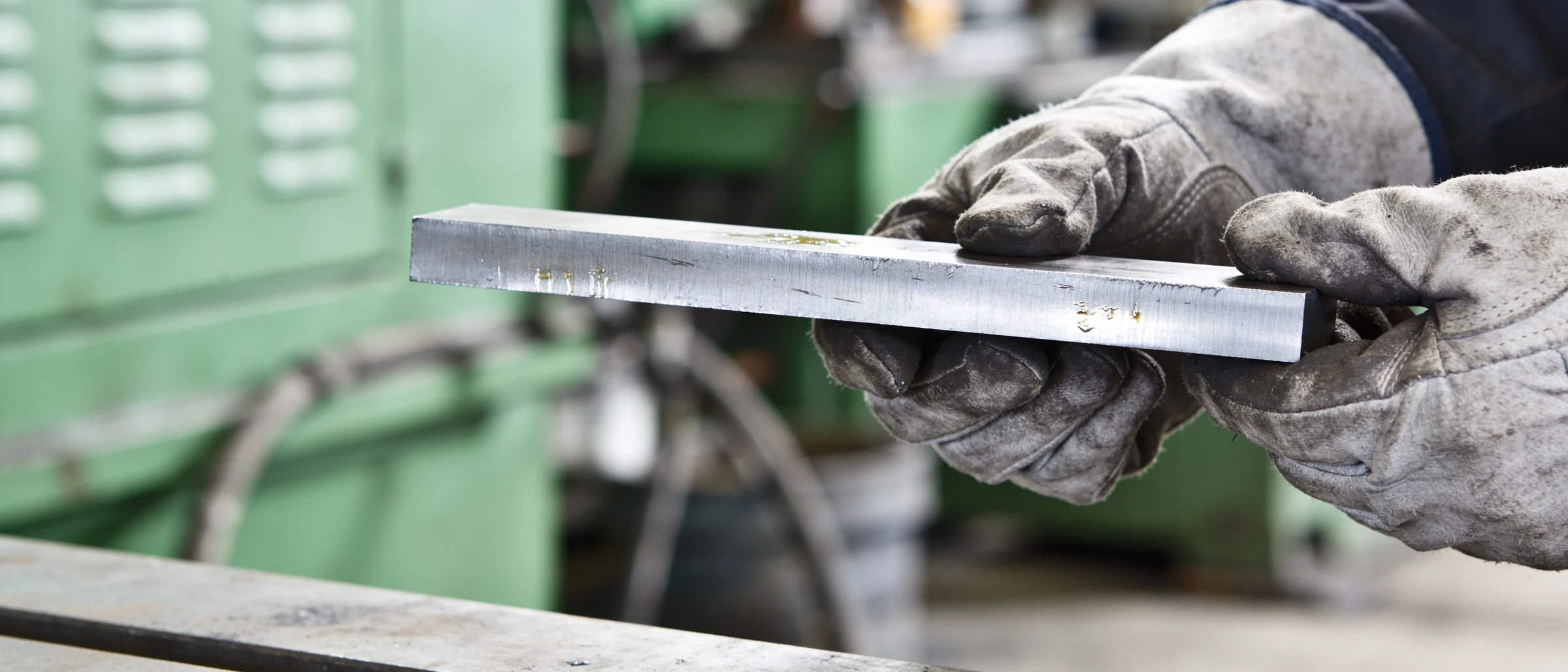 Hände in Arbeitshandschuhen halten ein Stück Flachstahl